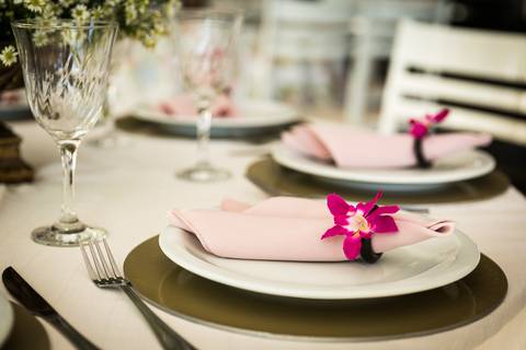 Fotografia de casamento com cerimônia e festa e recepção ao ar livre durante o dia no Califórnia Eventos em Araçatuba SP. Decoração da mesa do buffet com detalhe do prato, talheres e porta guardanapos com uma argola e flor.'