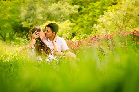 Foto do casal se beijando sentados no gramado com flores ao fundo em Maringá, PR'