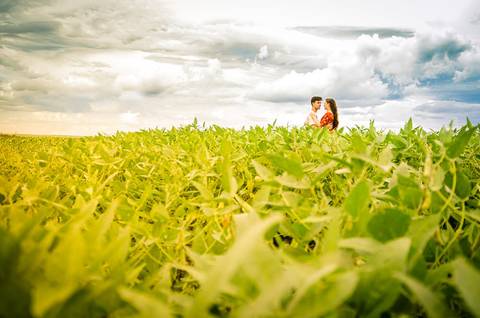 Fotografia do noivo e da noiva de se abraçando ao fundo em meio a uma plantação de soja com céu azul com algumas nuvens em Maringá, PR'
