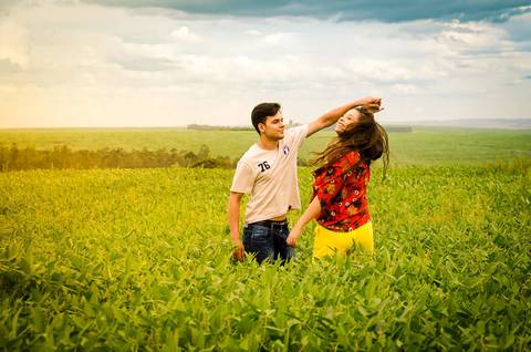 Fotografia do noivo e da noiva dançando em meio a uma plantação de soja com céu azul,  com algumas nuvens em Maringá, PR'