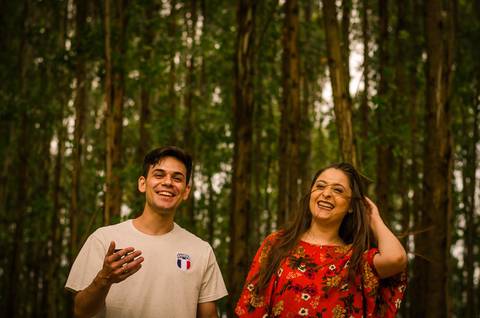 Fotografia do casal do noivo e da noiva no pre casamento de mãos dadas se divertindo e sorrindo. Ao fundo tem uma floresta de árvores altas em Maringá, PR'