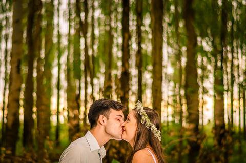 Foto do casal no pre casamento se beijando, ela com uma coroa de flores. Ao fundo uma floresta de árvores em Maringá, PR'