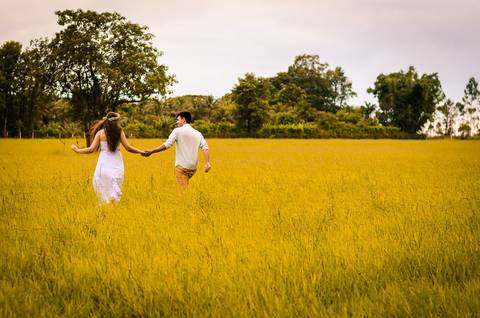 Fotografia do casal de noivos no pre casamento caminhando junto de mãos dadas em um gramado. O noivo e a noiva se olham. Em Maringá, PR'