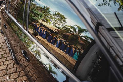 REFLEXO DOS PADRINHOS E MADRINHAS NO VIDRO DO CARRO NA ENTRADA DO CASAMENTO'