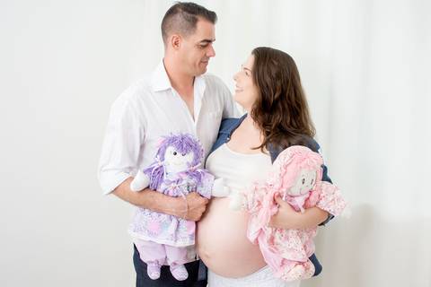 Adriana e seu marido abraçados com duas bonecas, uma boneca rosa outra lilas, e eles estão se olhando e sorrindo por nailie lucchesi e estudio amora'