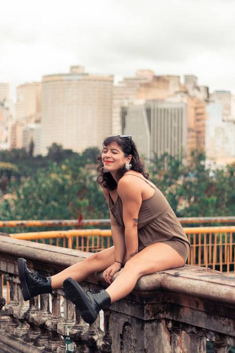 Modelo sentada em um parapeito com as pernas levantas e sorrindo. Fotos feitas em BH'