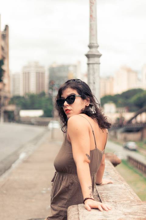 Modelo em pé em constada no parapeito com o olhar de cima dos ombros com o rosto sério e de óculos.  Rua Sapucaí'