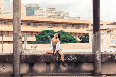 Modelo sentada no parapeito do viadulto santa tereza segurando a blusa e sorrindo de lado '