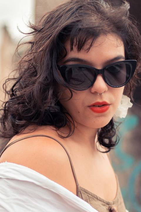 Retrato com modelo de olhando de lado, séria com óculos escuro, brincos grandes e cabelo solto'