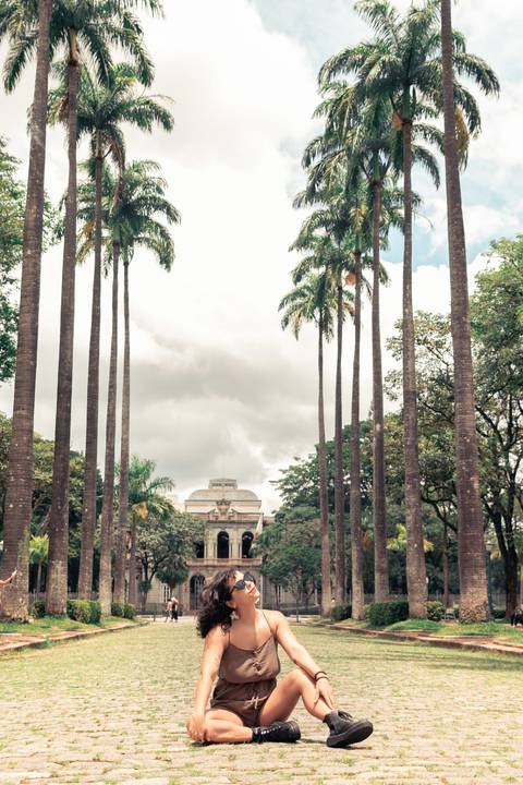 Retrato na Praça da liberdade, modelo sentada no meio da praça com os coqueiros e o palacio aparendo'