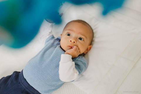 Bebê olhando para os brinquedos no berço com a mão na boca'