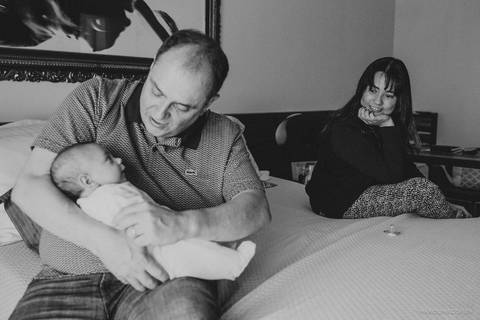 Mae sentada na cama, olhando o pai segurar o bebê'
