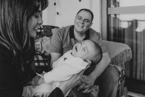 Fotografia de pai sorrindo ao ver a mãe com bebê no colo'