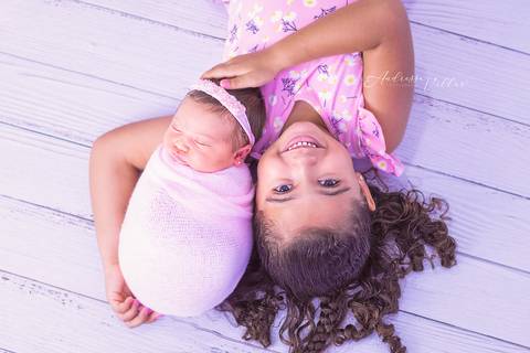 Recém nascida Giovanna enrolada no wrap rosa deitada com sua irmã mais velha com vestido rosa '