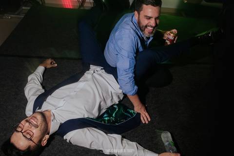 noivo deitado na pista de dança com padrinhos sentando nele'