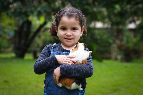 criança com porquinho da índia no colo, no quintal de casa'