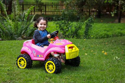menina brinca no seu carrinho rosa de pedal pelo gramado do jardim de casa'
