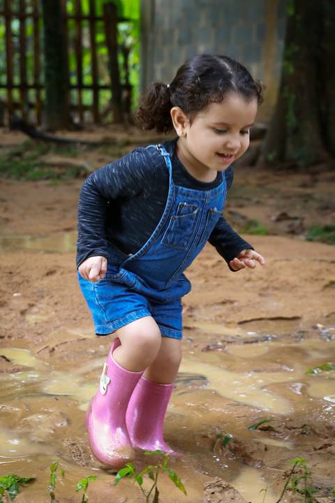 menina pula na lama para brincar, com suas botas de borracha cor de rosa'