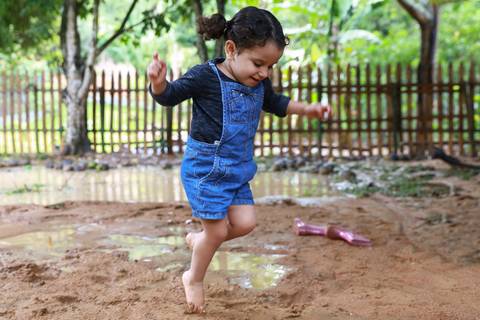 menina pula na poça de lama para brincar'