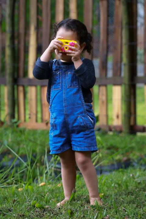 menina brinca com sua câmera fotográfica de brinquedo do outro lado do laguinho'