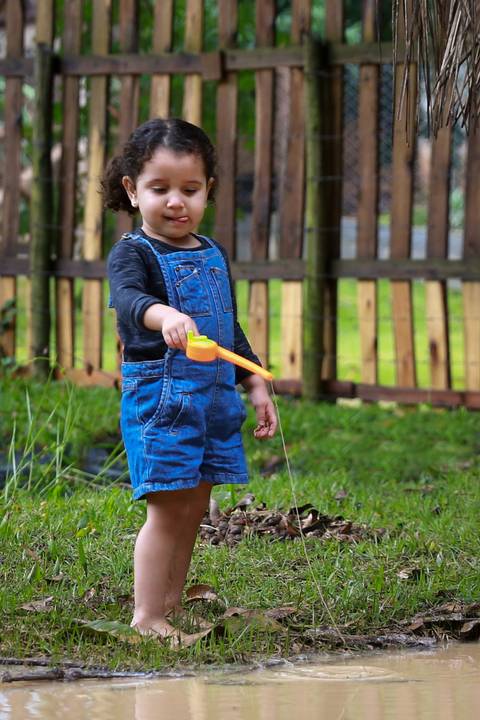 menina brinca com sua vara de pasca de brinquedo do outro lado do laguinho'