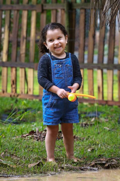 menina brinca com sua câmera fotográfica de brinquedo do outro lado do laguinho'