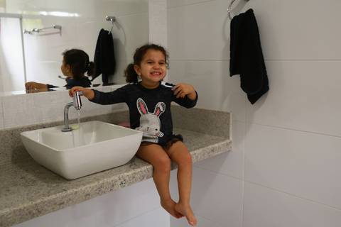 Menina sentada na pia do banheiro escova os dentes sozinha'