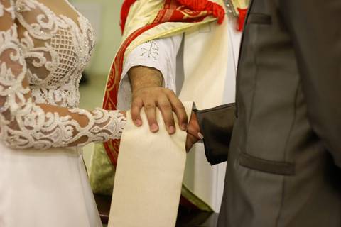 detalhe das mãos dos noivos sendo abençoadas pelo padre'