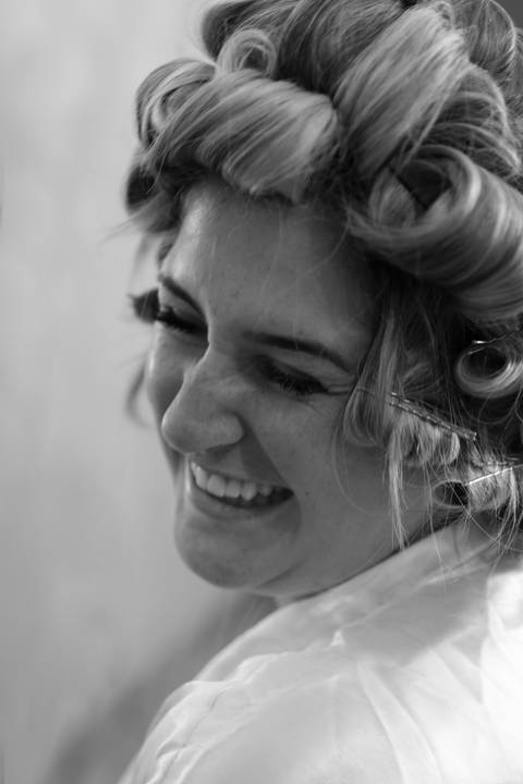 Noiva sorrindo de bobes nos cabelos durante o making of'