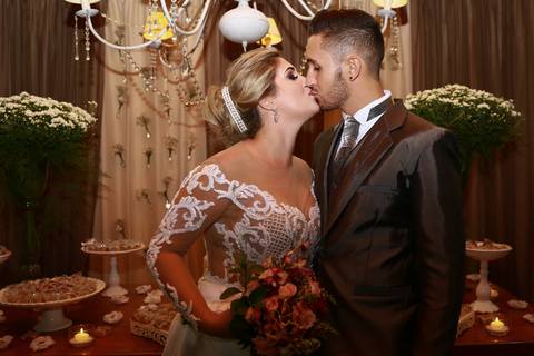 Noivos trocam beijo posado em frente a mesa do bolo'