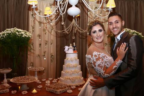 noivos posam em frente a mesa do bolo'