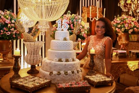 Aniversariante posa ao lado da mesa do bolo com decoração ao fundo.'