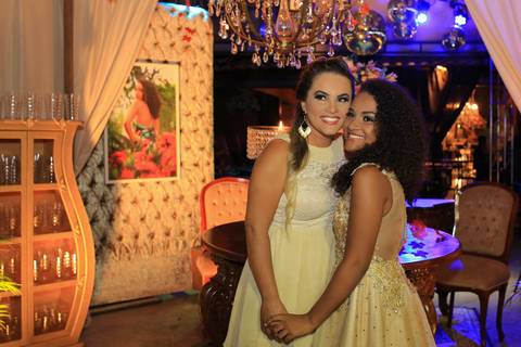 Aniversariante posa ao lado da mãe com decoração da festa ao fundo.'