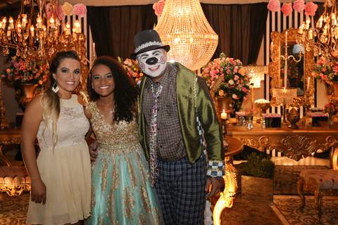 Aniversariante posa na mesa do bolo com sua mãe e o palhaço, celebrante da noite. Ao fundo decoração'