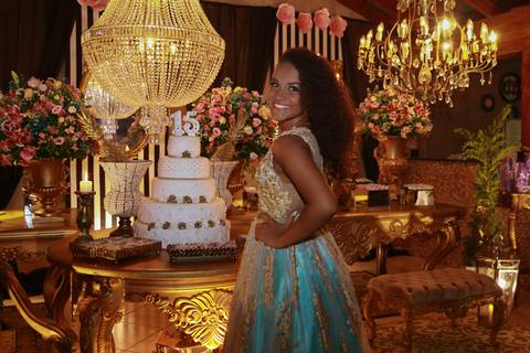 Aniversariante posa na mesa do bolo, de costas. Ao fundo decoração'