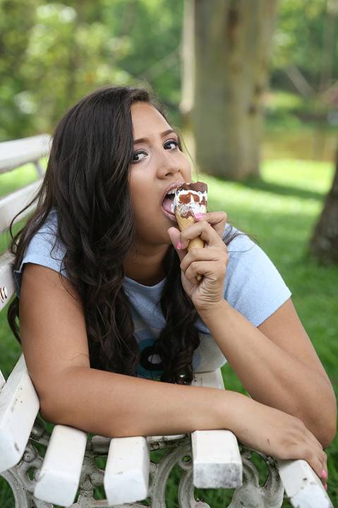 Debutante posa no banco de madeira, tomando sorvete'