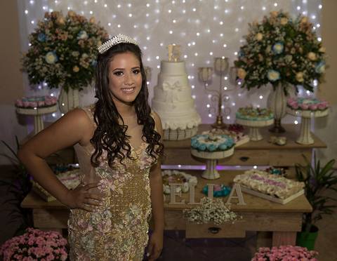 Debutante posa mostrando seu vestido em frente mesa principal da decoração'