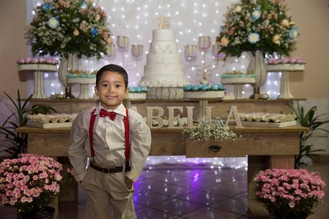 Garoto posa em frente mesa principal da decoração, de suspensórios e gravata borboleta'