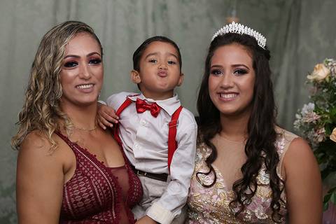 Debutante posa para fotos oficiais, com mãe e irmão, que faz bico para foto'