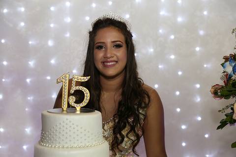 Debutante  posa na mesa do bolo, com detalhe da vela de aniversário'