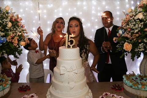 Debutante com seus pais e irmão, na mesa do bolo na hora do parabéns. Debutante assopra a vela'