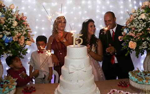 Debutante com seus pais e irmão, na mesa do bolo na hora do parabéns'