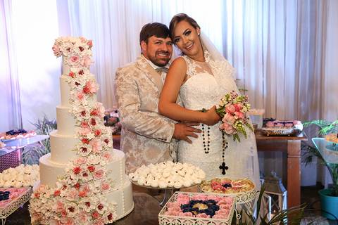 Noivos posam felizes e sorridentes na mesa do bolo'