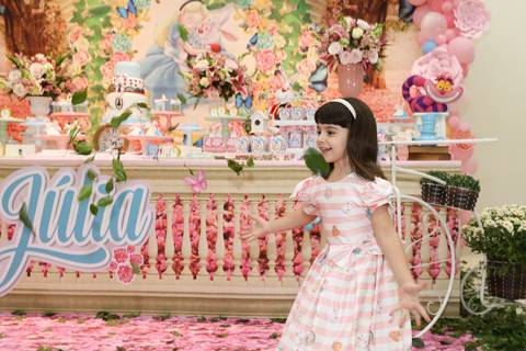 Aniversariante se diverte com chuva de folhas, da decoração, em frente a mesa do bolo'