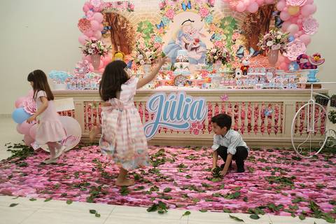 Aniversariante com os coleguinhas se diverte em chuva de folhas, da decoração, em frente a mesa do bolo'