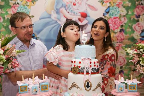 Aniversariante, junto com seu pai e sua mãe, cantam parabéns na mesa do bolo. aniversariante sopra a velinha do bolo enquanto seus pais comemoram'