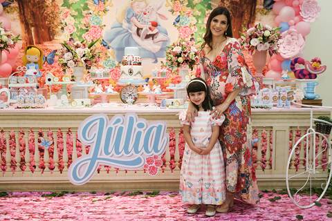 Aniversariante com a mãe posa na mesa do bolo para foto'