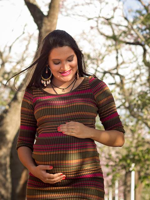 Gestante posa no parque, olhando para olhando, sorrindo e acariciando a barriga'