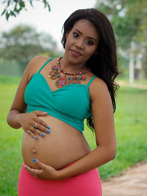 Gestante posa no parque, olhando para câmera e acariciando a barriga'