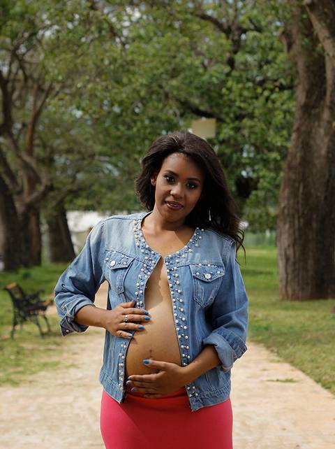 Gestante posa no parque, olhando para câmera e acariciando a barriga'